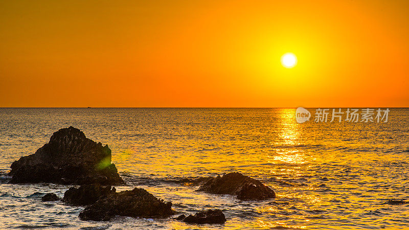 浪漫的观点，崎岖的岩石突出在海上与金色的日落天空