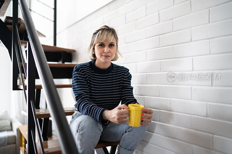 一个女人拿着茶杯坐在家里的楼梯上