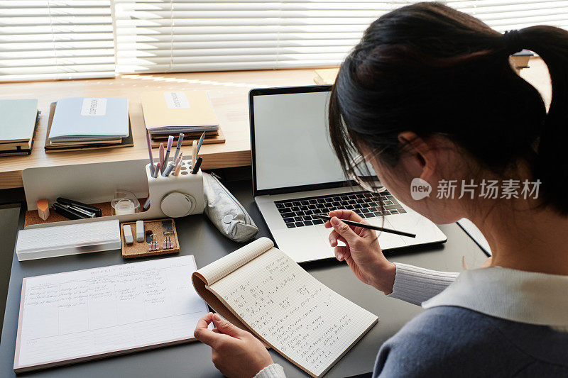 亚洲学生戴着眼镜，坐在桌边，一边做笔记，一边解数学题