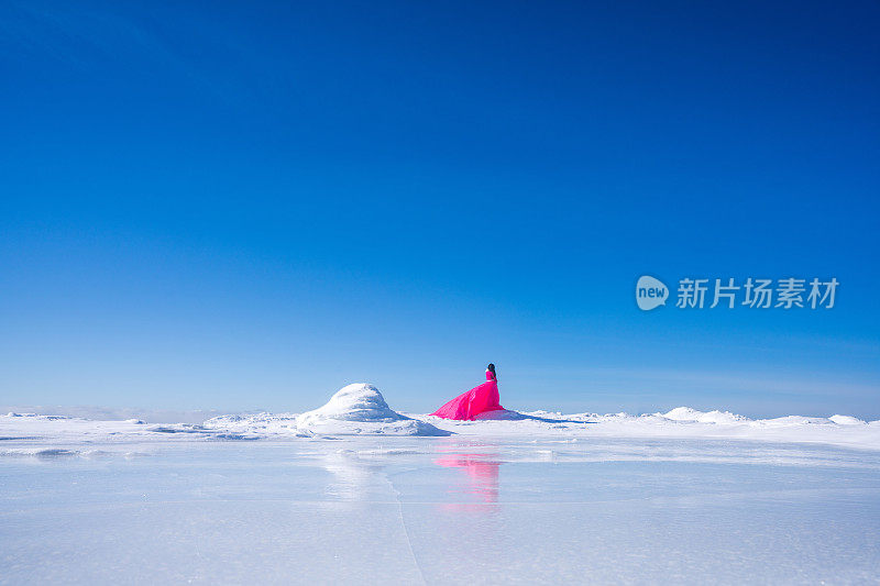 性感的模特穿着红色的连衣裙，背景河冰水石冷暴风雪降雪。