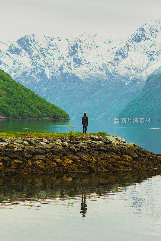 挪威山脉背景下的男子剪影。美丽的峡湾景观。游客站在盖朗峡湾前。雪在山上。斯堪的那维亚。北自然。Experiental旅行。假期