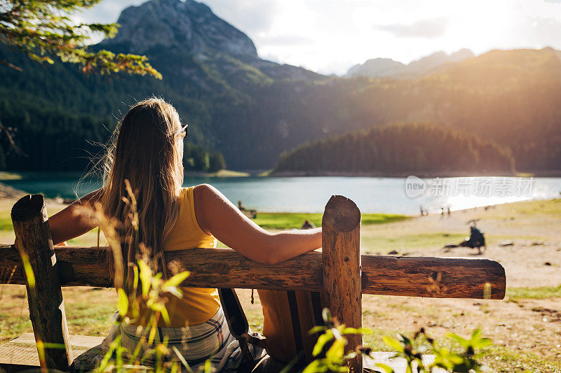 一位穿着黄色t恤的陌生女子坐在木凳上，享受着山上的大自然。