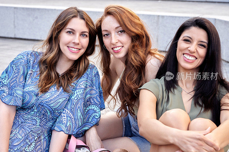 三位女性朋友坐在户外，看着镜头微笑。