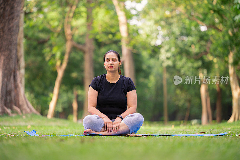 一个女人在公园里做瑜伽，坐在瑜伽垫上