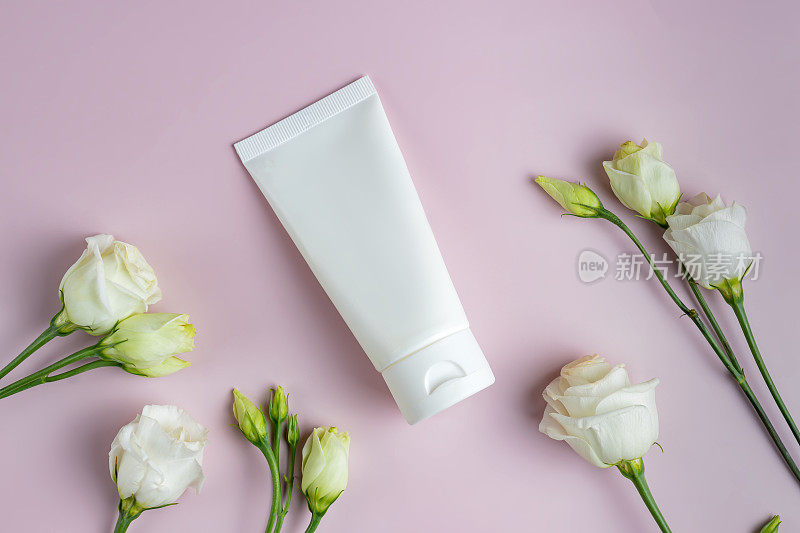 白色的空白塑料管，用于装面霜、面膜、洗发水或牙膏，粉色的背景上有菊花花。春季化妆品包装呈现。模型