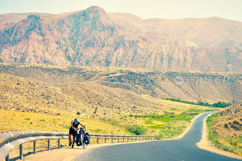一名白人骑自行车的男子推着他沉重的旅行自行车上山，在极端炎热的户外山区。自行车旅游冒险生活理念。艰难的上山周期和决心