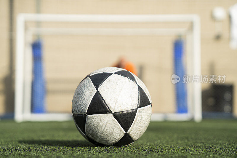 足球躺在球场的草坪上，门将站在后面