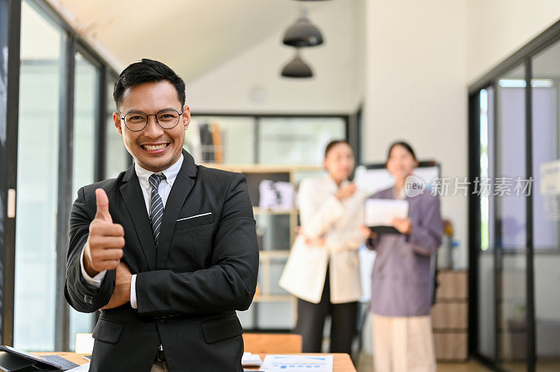 专业的成年亚裔男性老板站在他的办公楼里竖起大拇指
