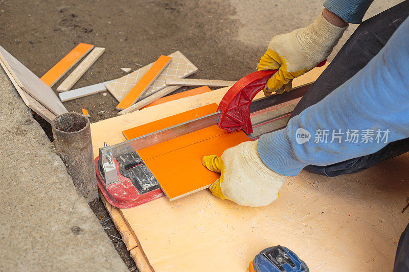 手动瓷砖切割机。一名工人用切割器切割瓷砖。瓷砖铺设。构造和修理的概念。