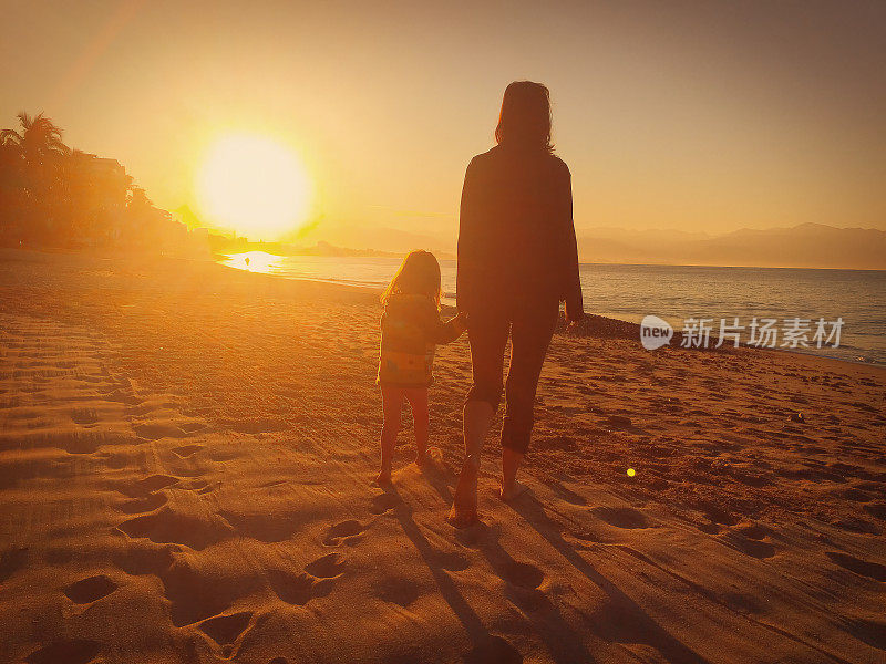 日落时分，妈妈和女儿手牵着手沿着海滩散步。
