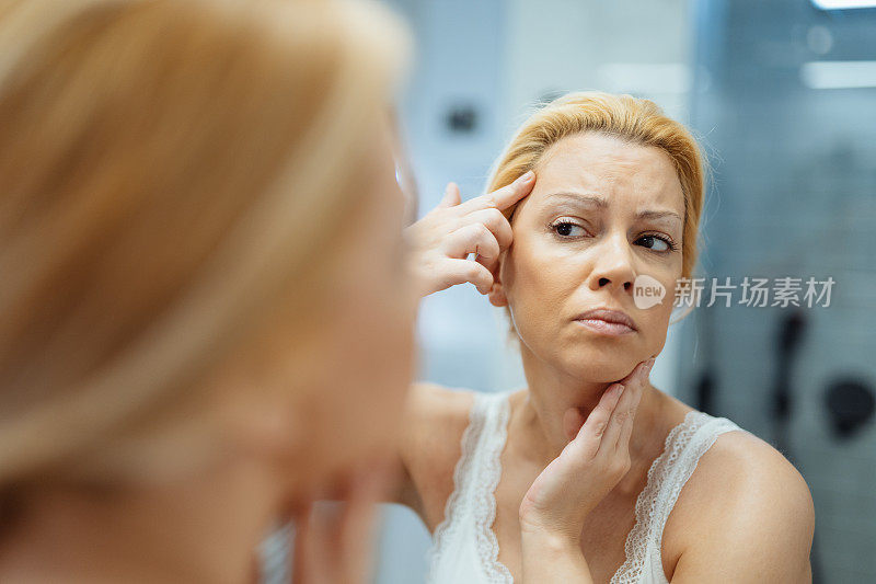 成熟的女人在浴室的镜子前，分析她的脸和皱纹