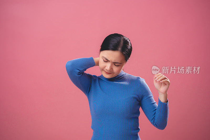 一名亚洲妇女颈部疼痛，孤立地站在粉红色的背景上。