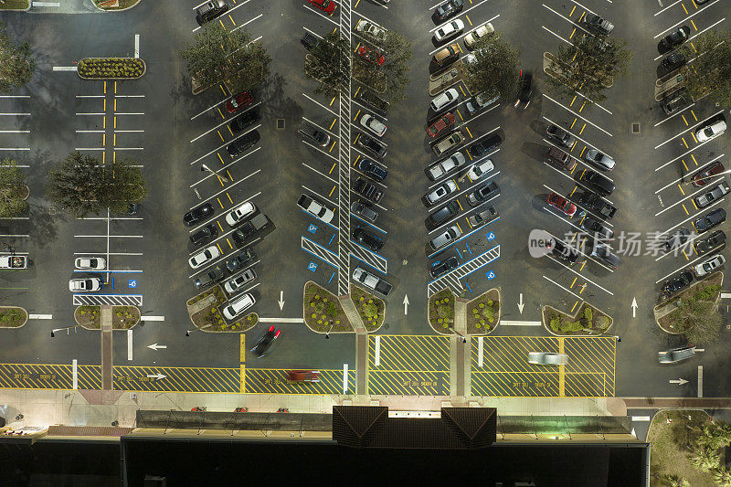俯视图，许多汽车停在夜间照明明亮的停车场前的杂货店购物中心。消费主义与市场经济的概念