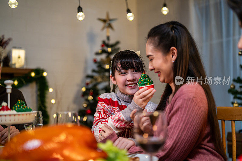亚洲可爱的家庭在家里一起庆祝圣诞派对。迷人的父母和亲戚们在家里的餐桌上吃着感恩节大餐，庆祝圣诞前夜的节日。