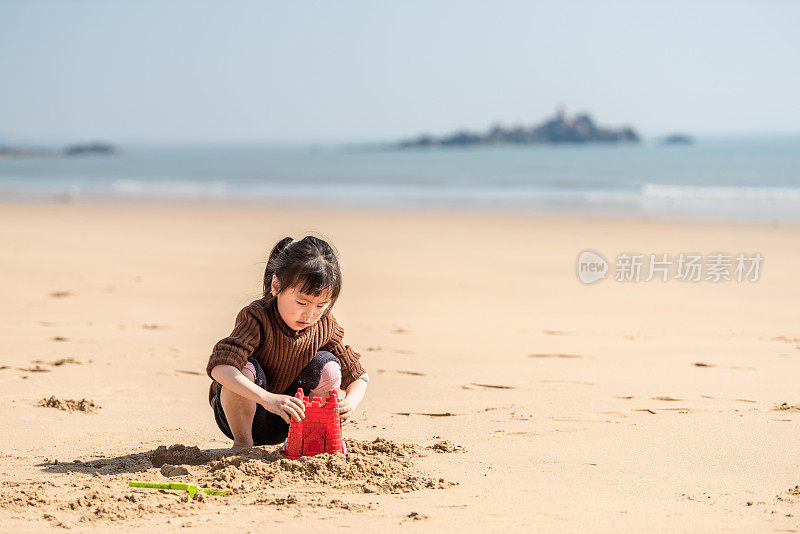 一个中国小女孩在沙滩上玩沙子