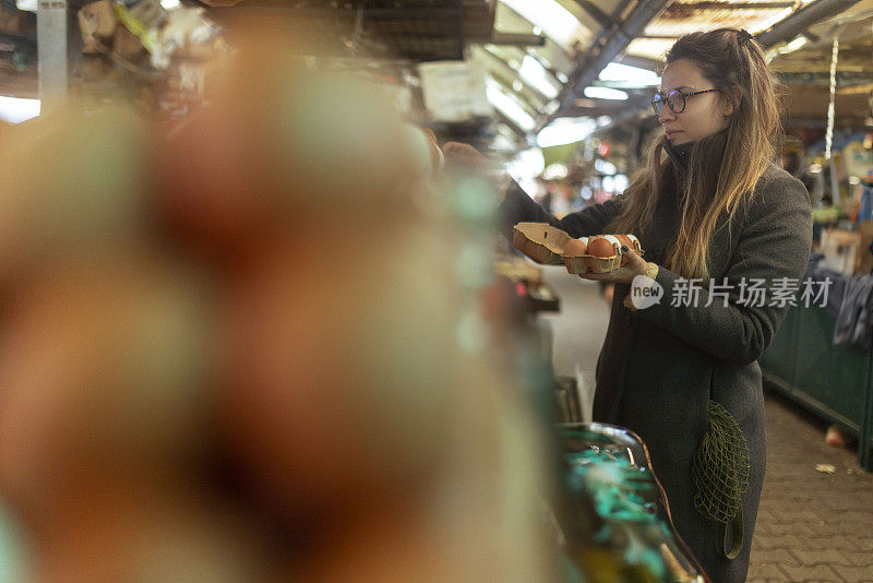 可爱的女人在街市上买鸡蛋。她把它们放在一个纸板蛋盒里