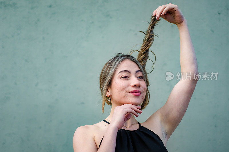 美丽的年轻女子的肖像玩她的头发在灰色背景