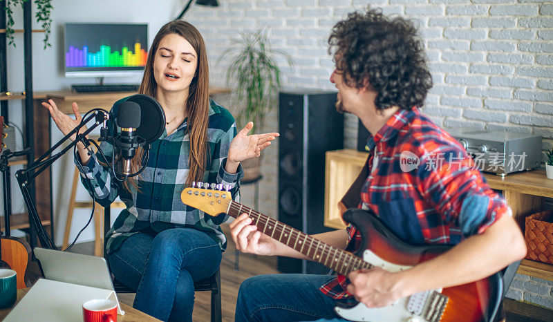 在家庭音乐录音室里，当吉他手弹吉他时，年轻女子对着麦克风唱歌