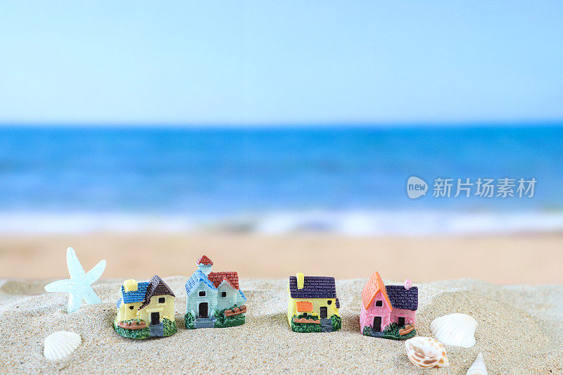 一排模型度假小屋站在阳光明媚的沙滩上，背景是退潮时的海浪，海星，贝壳，大海和海岸线，度假租赁和度假屋的概念，重点放在前景，复制空间