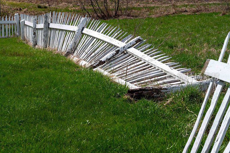 白色的尖桩篱笆和腐烂的柱子躺在绿色的草地上