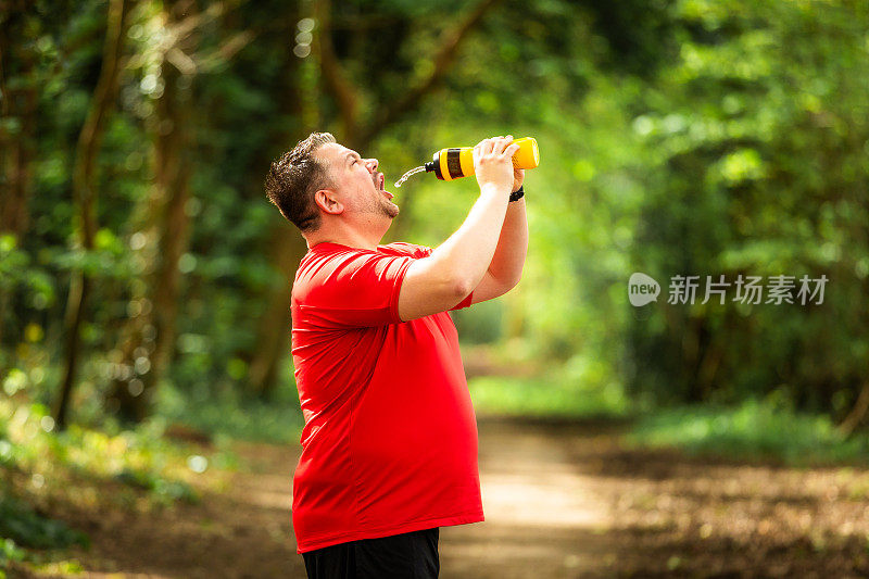 疲惫的男性慢跑者在森林里从瓶子里喷水