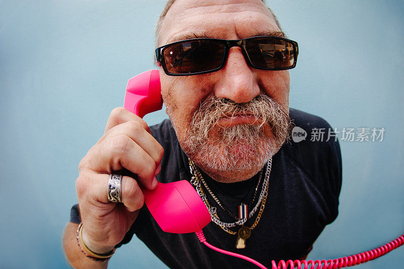 滑稽愤怒的高级男子拿着粉红色的手机听筒