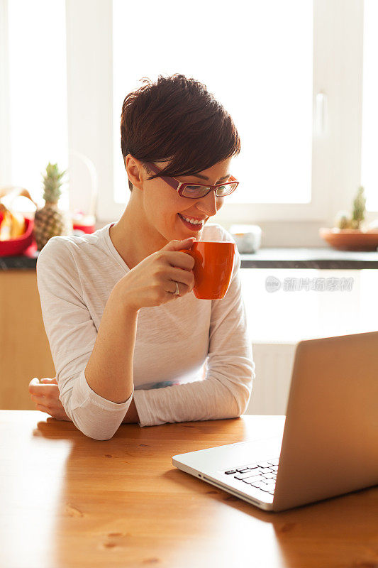 年轻漂亮的女人在厨房用笔记本电脑喝咖啡
