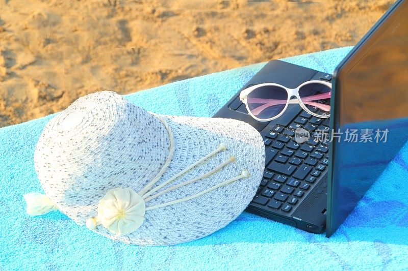 笔记本电脑，太阳镜和太阳帽在海滩上