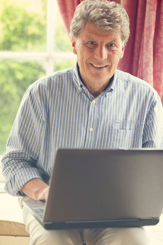 成熟微笑的男人坐在他的凸窗边使用笔记本电脑