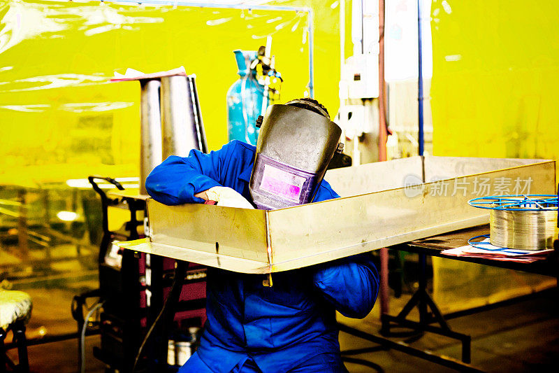 在钢铁厂的零件上工作的掩膜焊工