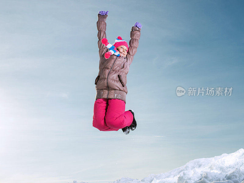 快乐的女孩在雪地上玩得很开心，跳得很高。