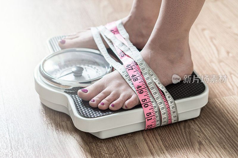 厌食症和饮食失调的概念。双脚用卷尺绑在秤上。对减肥上瘾和痴迷。