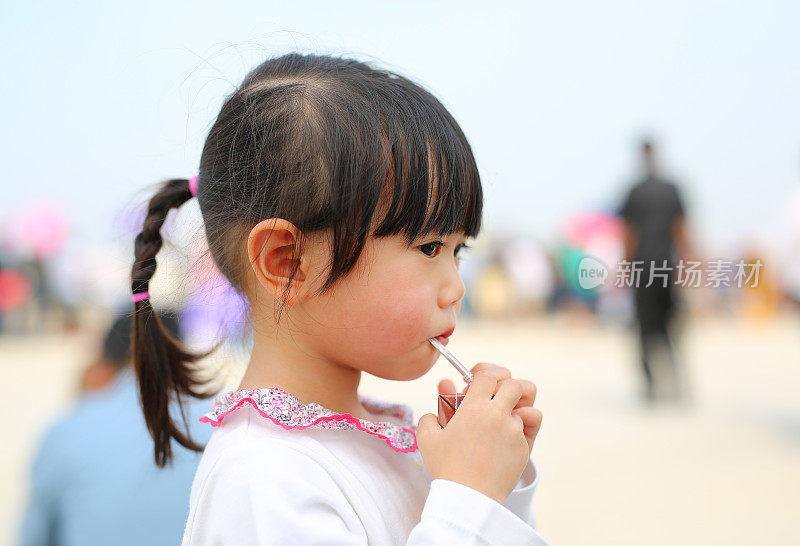小女孩用吸管喝牛奶的特写。肖像户外。