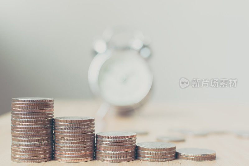 概念商业金融省钱，硬币堆放在木桌上和模糊的闹钟