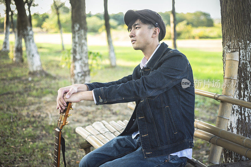 沉思的年轻人坐在木凳上，手里拿着吉他