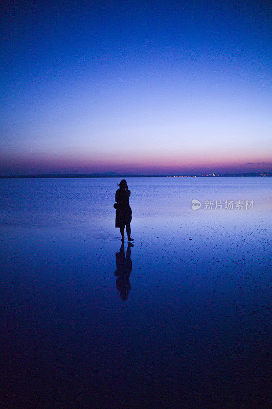 一名女子站在土耳其科尼亚的盐湖上，夕阳西下