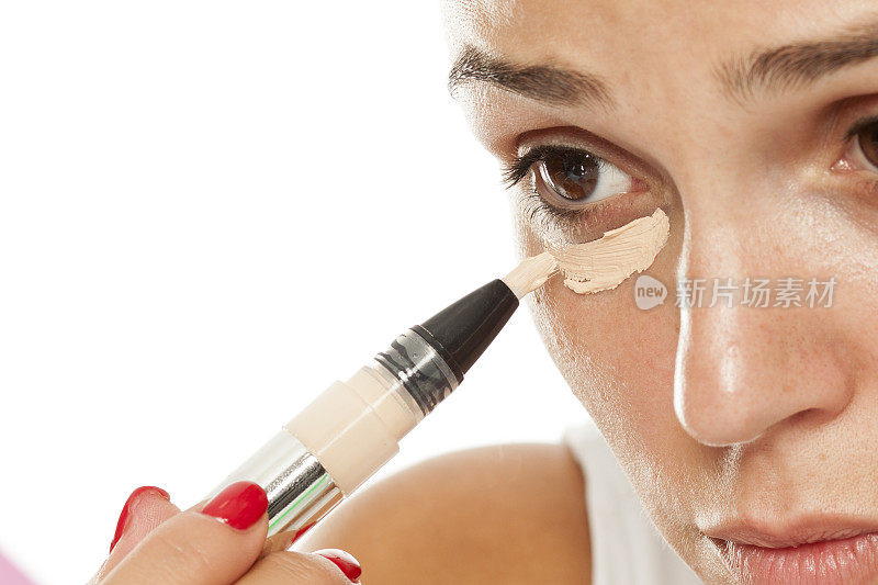 年轻妇女用点妆器把遮瑕膏涂在眼睛下面