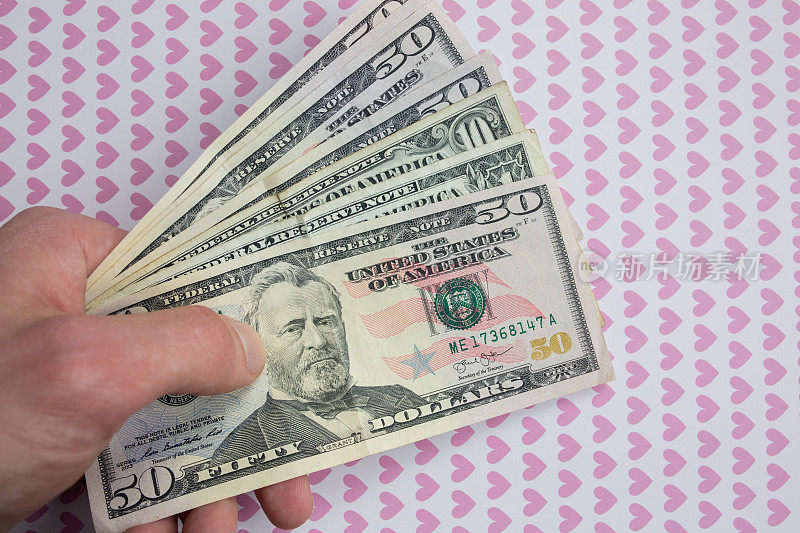 背景上的男人手里拿着钱，上面画着粉色的心。爱的美元。是时候去购物买东西了。钱购物狂上瘾。
