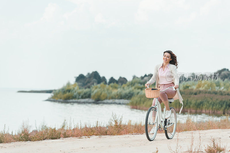 微笑的女人在沙滩上骑复古自行车