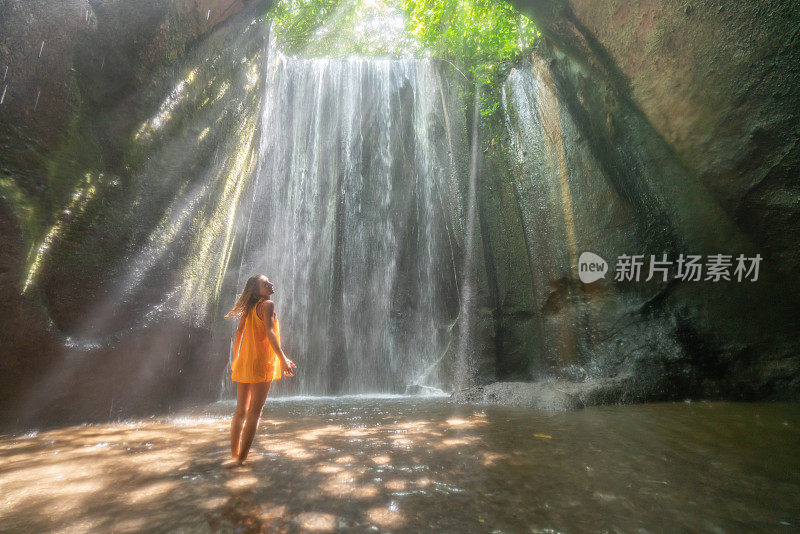 穿着黄色衣服的女孩站在热带雨林的洞穴里，仰望着从岩石上射下来的壮观的阳光。人们旅行的奇妙欲望自然的概念