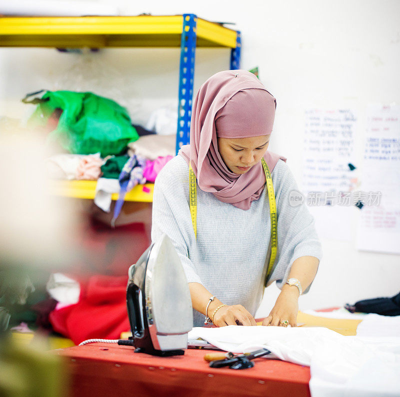 穆斯林女服装设计师在车间裁剪有图案的纺织品