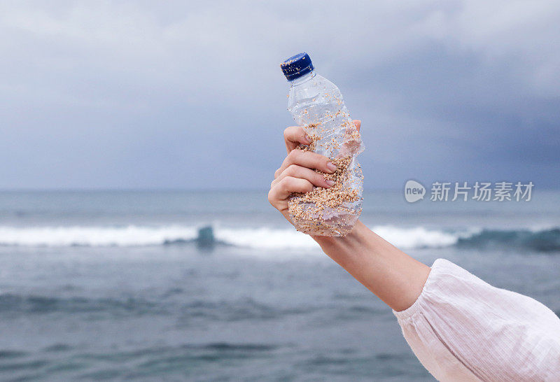 蓝天背景下，手里拿着一个塑料瓶。从海滩上收集垃圾的行动。Trash-free海域概念。一次性塑料是人类的嗜好，它正在破坏我们的计划