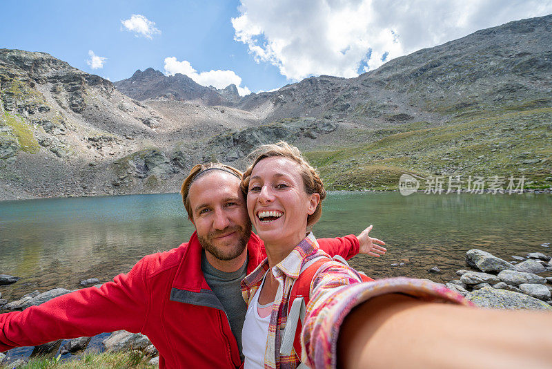 年轻的情侣徒步旅行在山湖边远足时拍自拍照