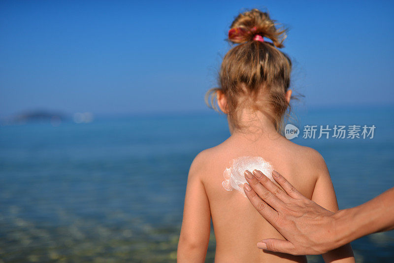 母亲在热带海滩上给女儿涂防晒霜