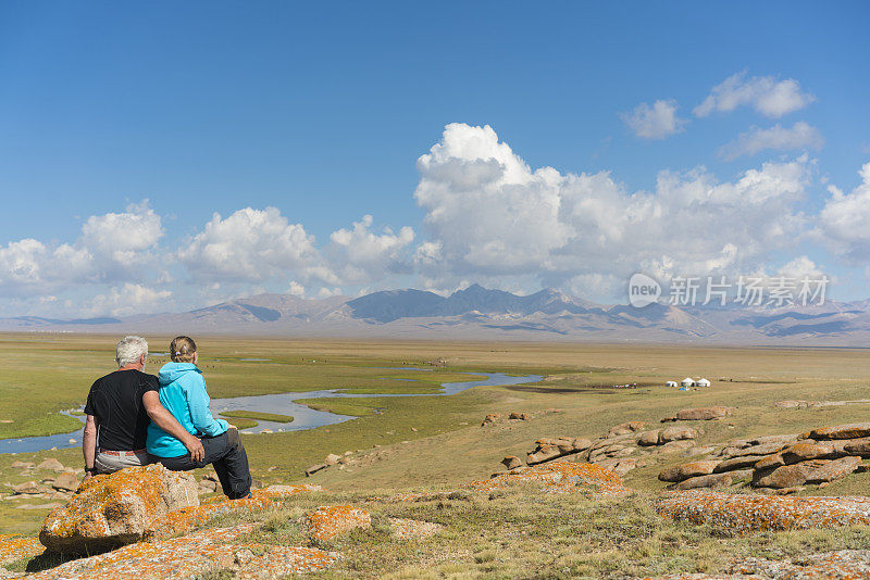 在吉尔吉斯斯坦，一对老年夫妇互相抱着看风景优美的乡村风景