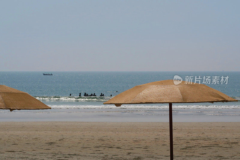 在印度果阿的帕洛伦海滩，棕色的海滩阳伞，度假者，游客和海滩游客在热带冬季度假，日光浴，在海里游泳