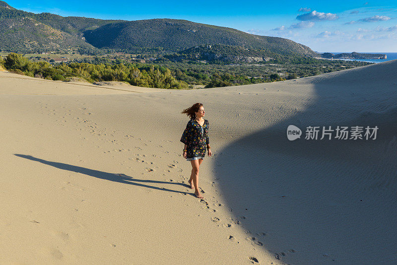 一个年轻漂亮的女人走在沙丘上。