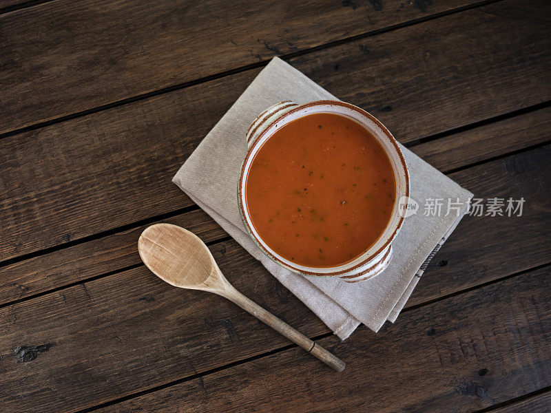 一碗西红柿罗勒汤，放在一个乡村碗里，靠在一张古老的深色木制桌子上。