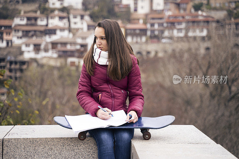 青少年的精神。美丽的十几岁的女孩在一个漫长的学校一天后，带着滑板在户外做作业。