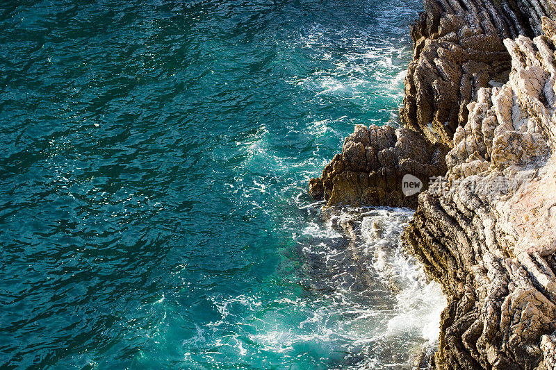 海浪拍打着岩石峭壁，在深蓝色的海水上溅起白色的浪花和泡沫。